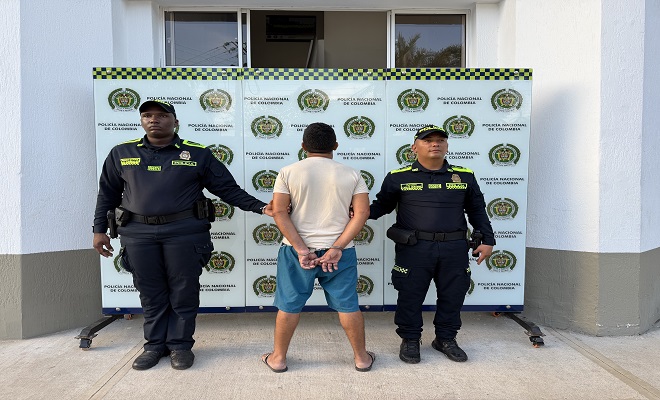 Una persona de espalda capturado por el delito de violencia intrafamiliar, rodeado de dos Policías brindando seguridad 