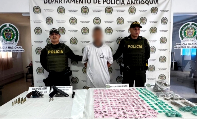 Dos policías custodiando a un capturado con droga y armamento