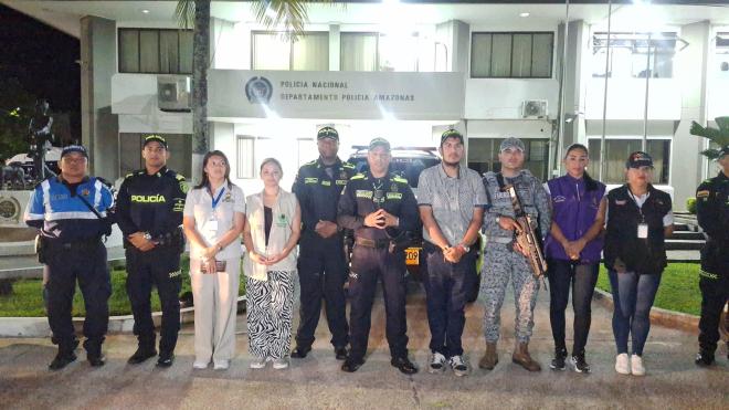 Tres policías y un miembro de la Fuerza Aérea de Colombia de pie acompañados por funcionarios con camisas de distintos colores