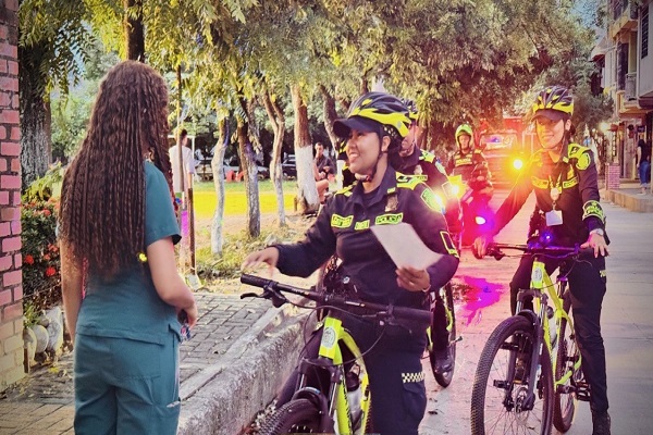 Tres Policías de patrulla purpura en campañas preventivas, una Policía entregando volante a una ciudadana 