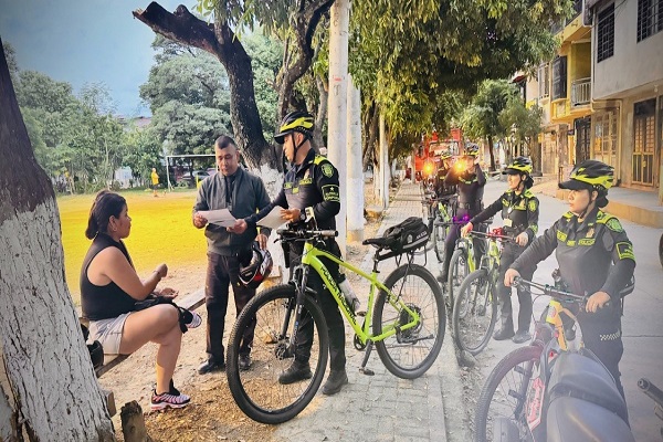 Cinco Policías de patrulla purpura en campañas y un funcionario entregando volante informativo a dos ciudadanos