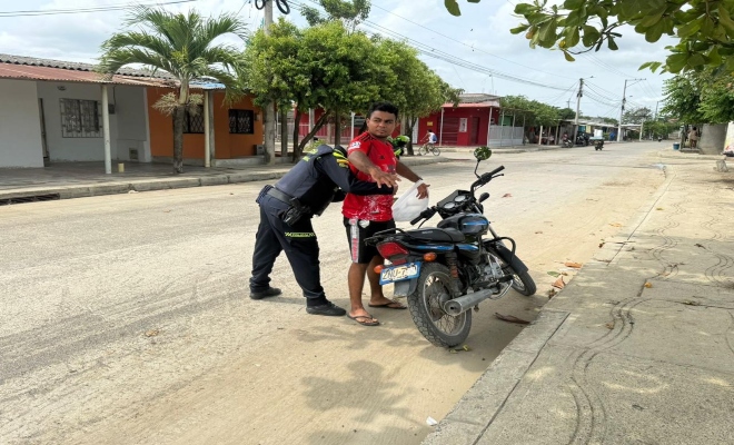 Un policia realizando registro a un ciudadano y una motocicleta 