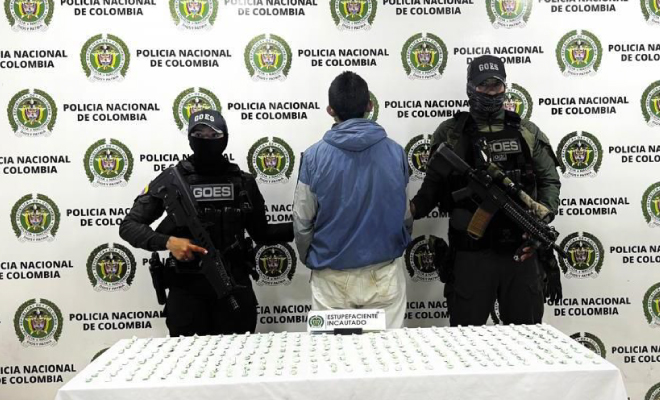 Hombre capturado en medio de dos Policías, en frente se encuentra ubicada una mesa con dosis de bazuco incautado