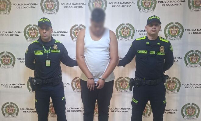 En un espacio institucional, una persona con el rostro difuminado se encuentra de pie entre dos integrantes de la Policía Nacional. 