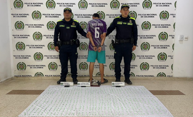 Hombre capturado en medio de dos policías, en frente elementos incautados