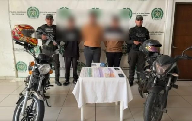 Hombres capturados en medio de dos polic&iacute;as, en frente dinero recuperado y a los lados motocicletas inmovilizadas