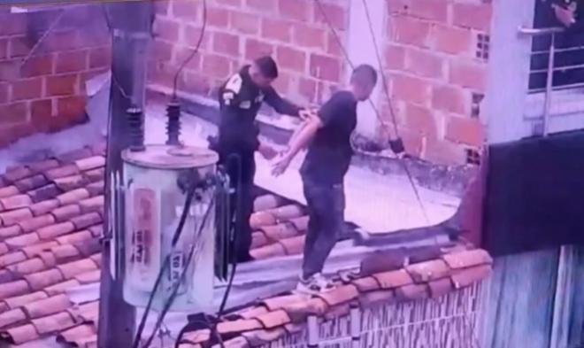 Un policía y una persona capturada sobre los techos de algunas viviendas. En la escena se observa un transformador eléctrico y cables cercanos