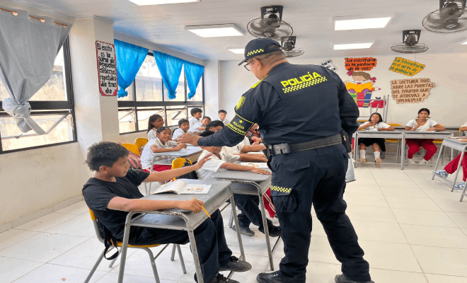 Varios estudiantes están sentados alrededor de una mesa en sus sillas, con un policía de pie frente a ellos