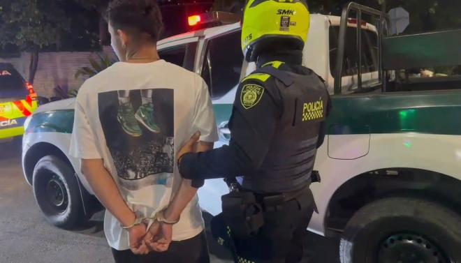 hombre capturado de camiseta blanca camina junto a un policía hacia una patrulla