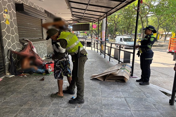 Dos Policías y uno de ellos realizando registro a persona a una personas en condición de calle